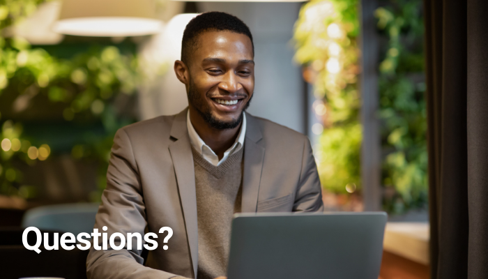 Smiling man in a suit working on a laptop with the word “Questions?” overlaid.