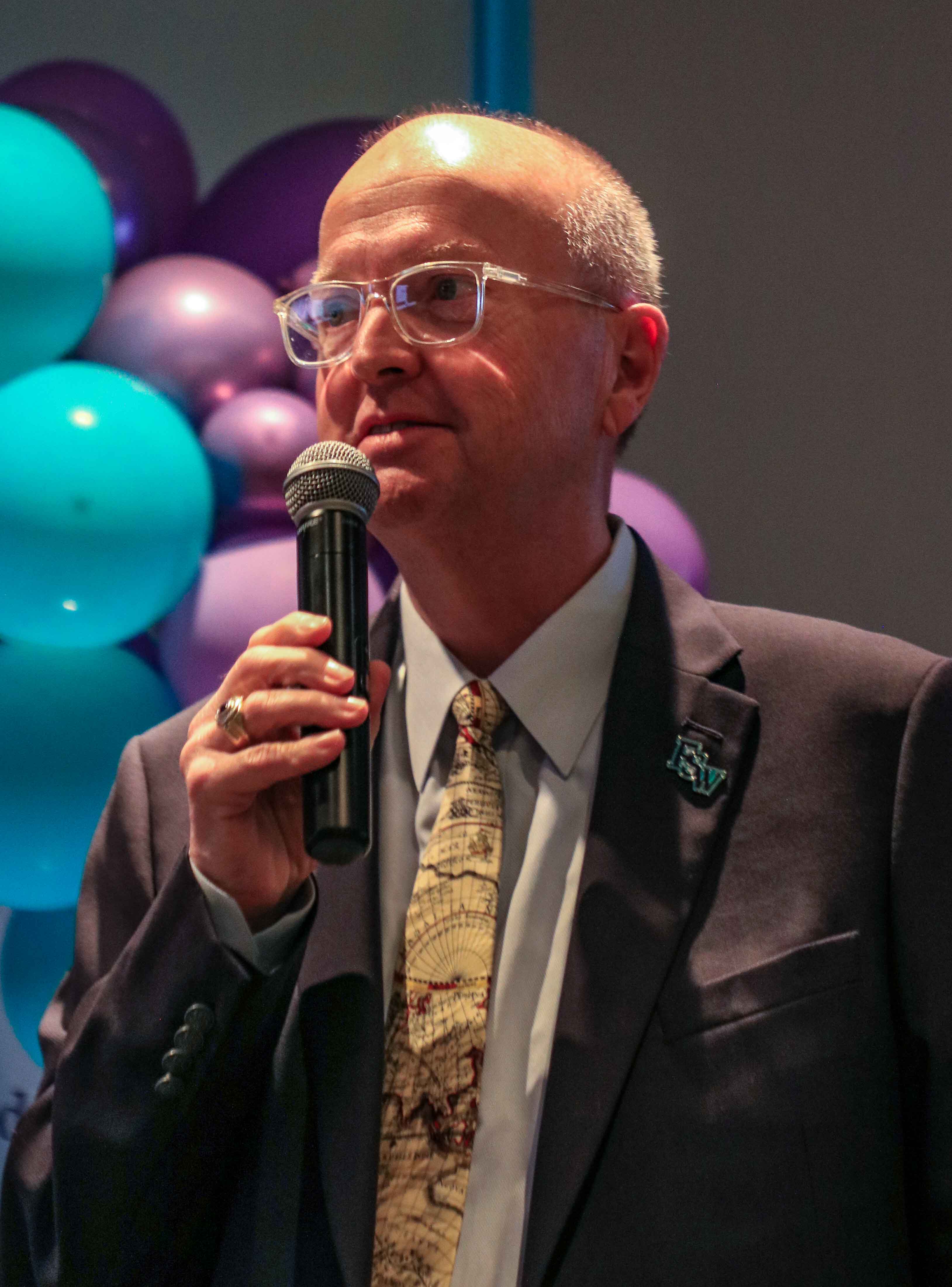 With purple and aqua balloons in the background, FSW President Dr. Jeff Allbritten holds a microphone while presenting at the Lee Campus Life Awards on April 15, 2026.