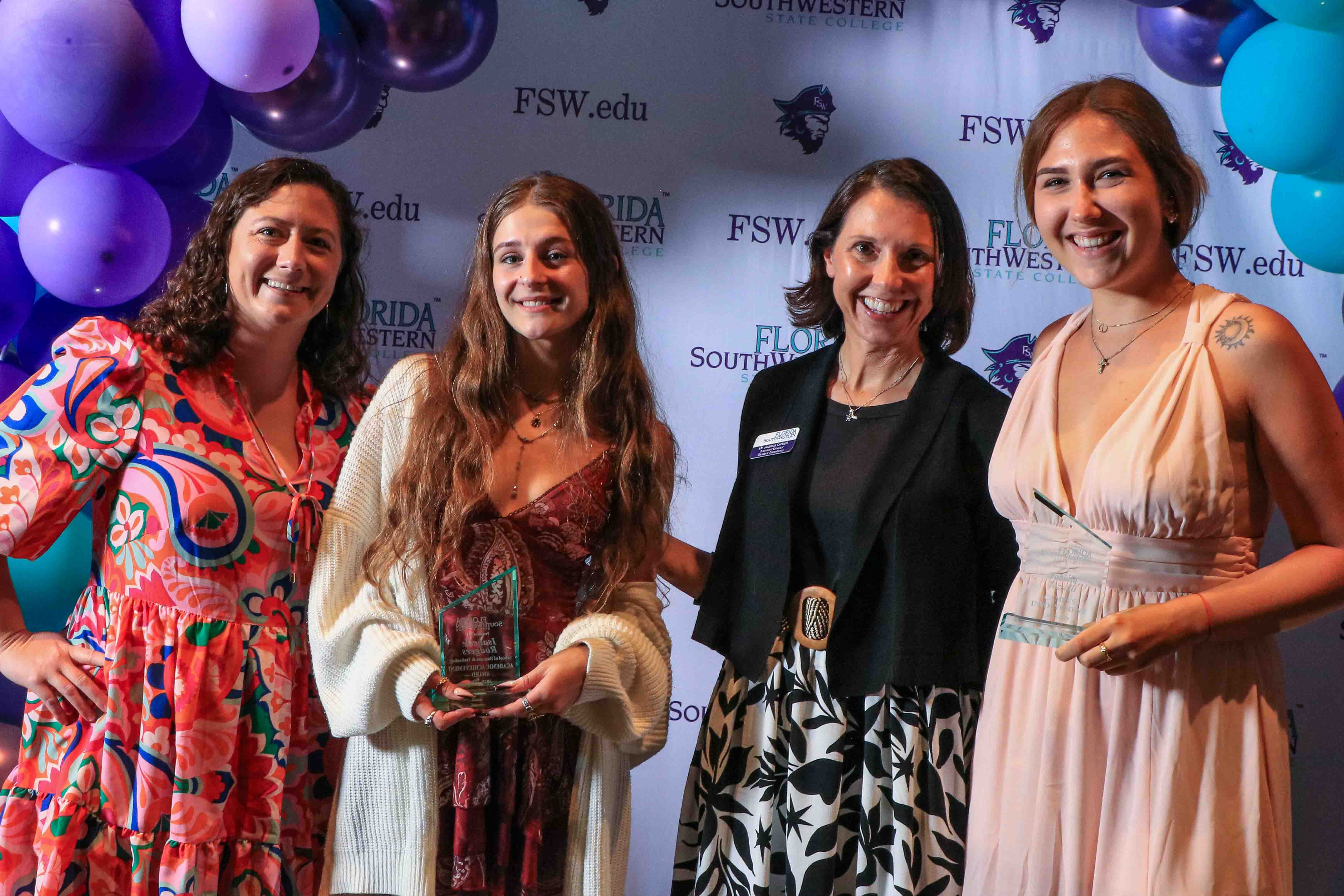 Student award winners and supportive staff pose in front of a backdrop of purple and aqua balloons and a banner with FSW logos and fsw.edu.