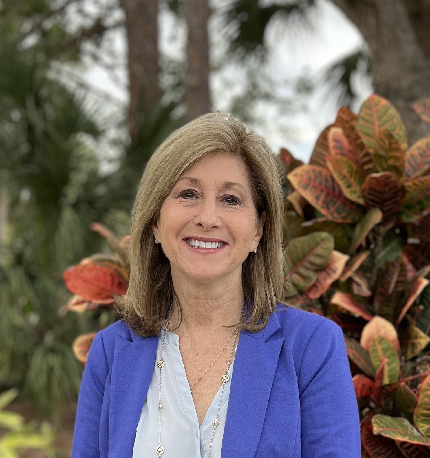 A headshot of Dr. Susan Holland, a smiling woman outdoors in a blue blazer.