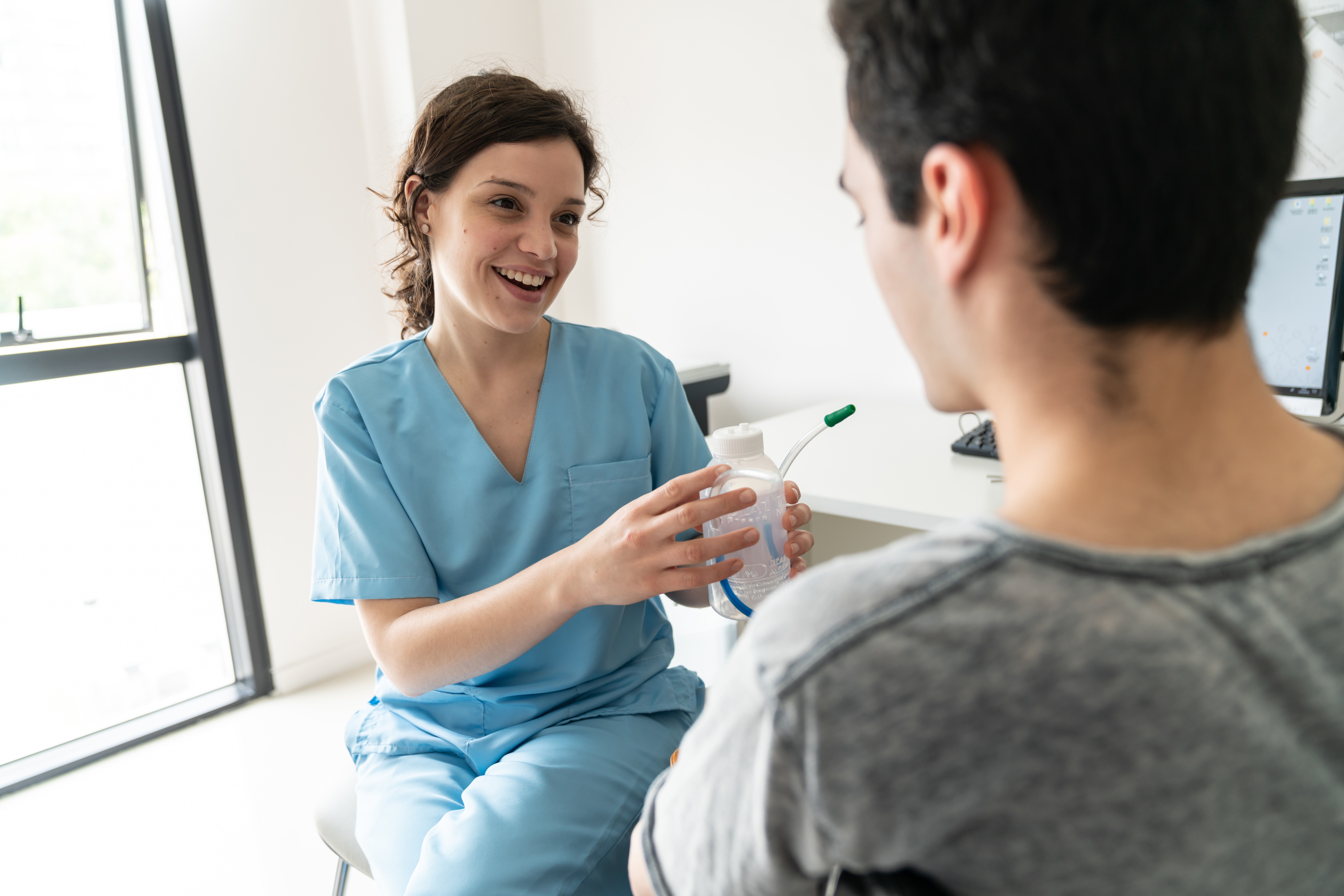 Respiratory therapist talking to male patient while holding a spirometer.