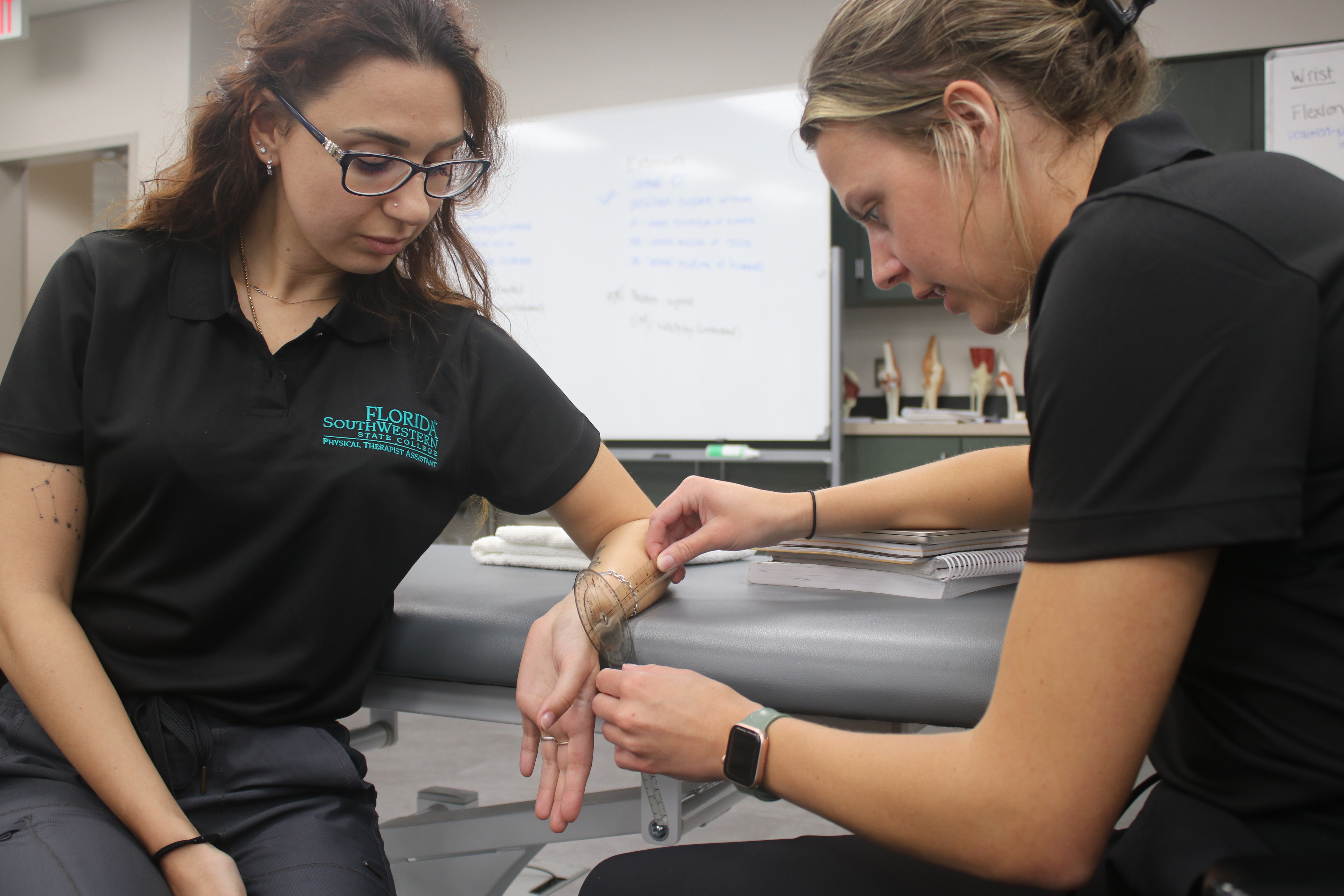 Two FSW Physical Therapist Assistant students practice measuring wrist movement with a goniometer in a classroom.