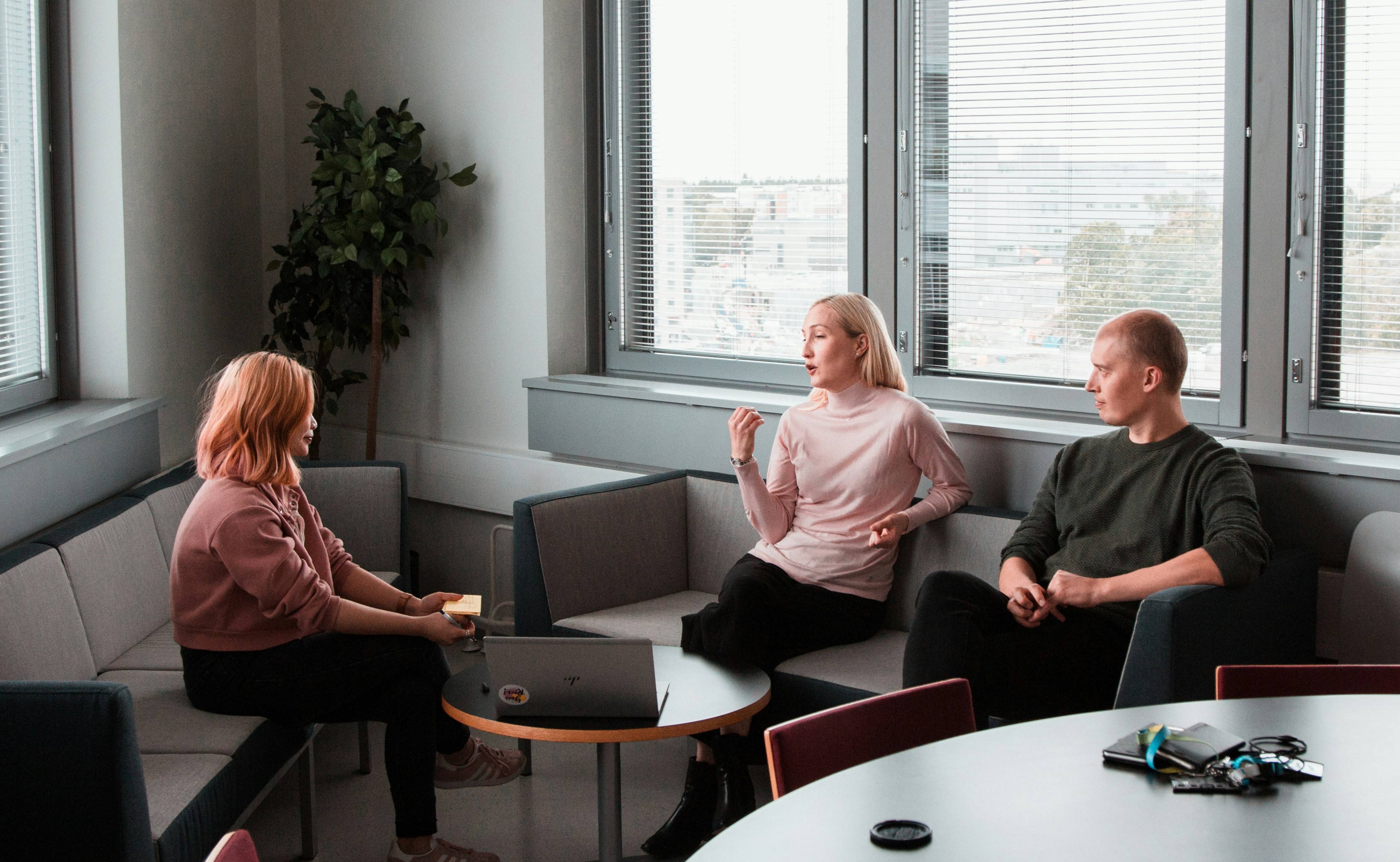 Three individuals sit in a circle on modern couches during a daytime therapy session in a well-lit room with large windows.