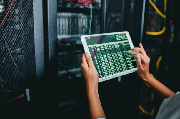 Technician using a tablet to monitor data in front of a server rack.