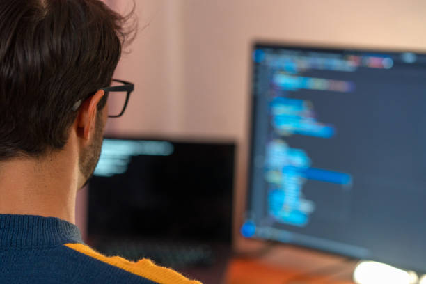 Person coding on a computer with a blurred screen showing code in a dark-themed text editor.