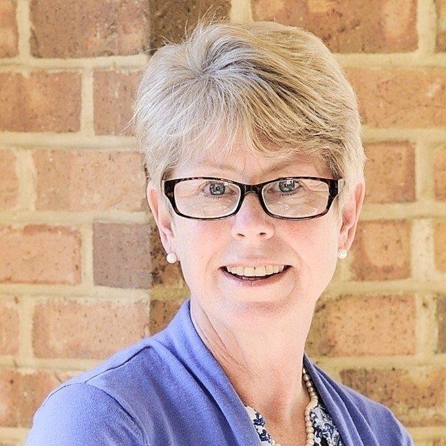 Headshot of Dr. Mary Catherine Faust. She has short hair, wears glasses, and is dressed in a purple cardigan.